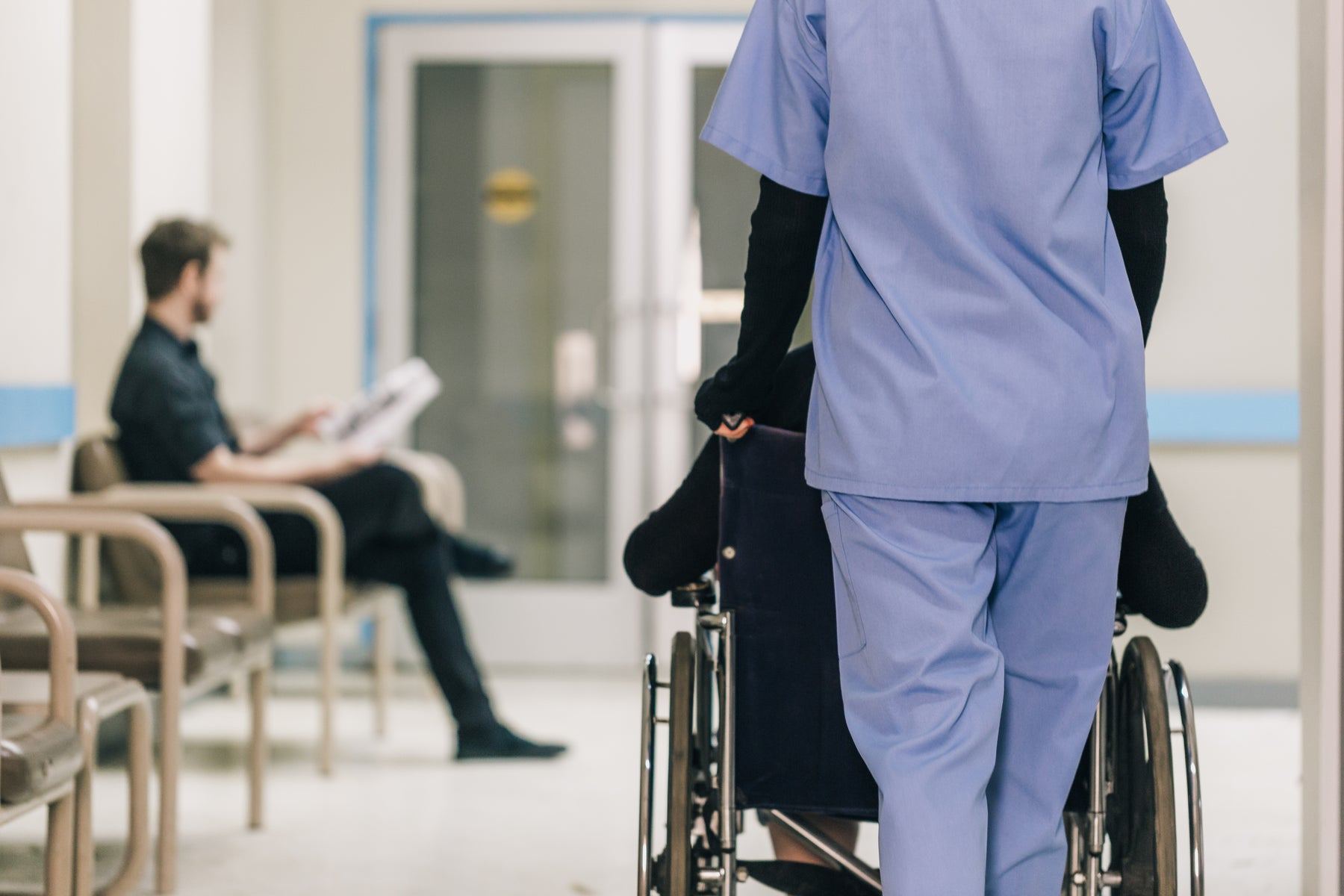 A nurse pushing a patient in a wheelchair down a hospital corridor